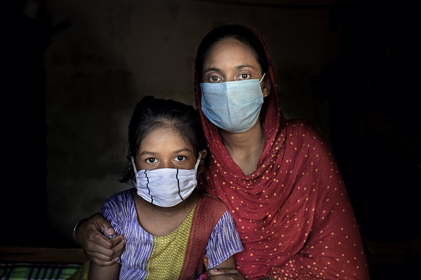 A woman and her daughter wearing masks, looking at the camera.